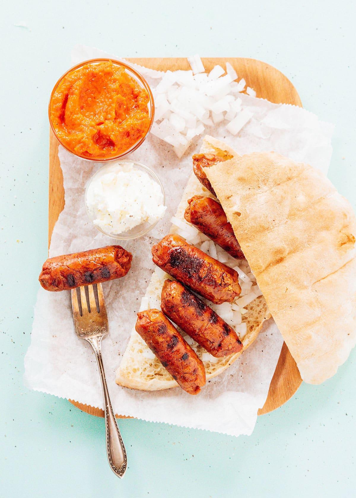 Vegetarische Cevapcici (Kroatisches Cevapi-Sandwich-Rezept) 2 Vegetarische Cevapi auf einem Teller mit Ajvar und Kajmak angerichtet.