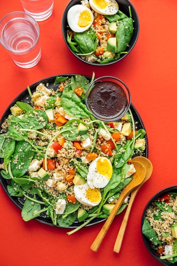 Spinat-Quinoa-Salat mit Balsamico-Vinaigrette 2 Mediterraner Quinoa-Salat auf einem Teller mit Servierlöffeln, ansprechend angerichtet
