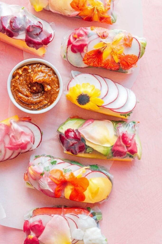 Essblumen-Frühlingsrollen 2 Mandelbutter-Dip-Schale neben acht essbaren Blüten-Sommerrollen auf rosafarbenem Hintergrund