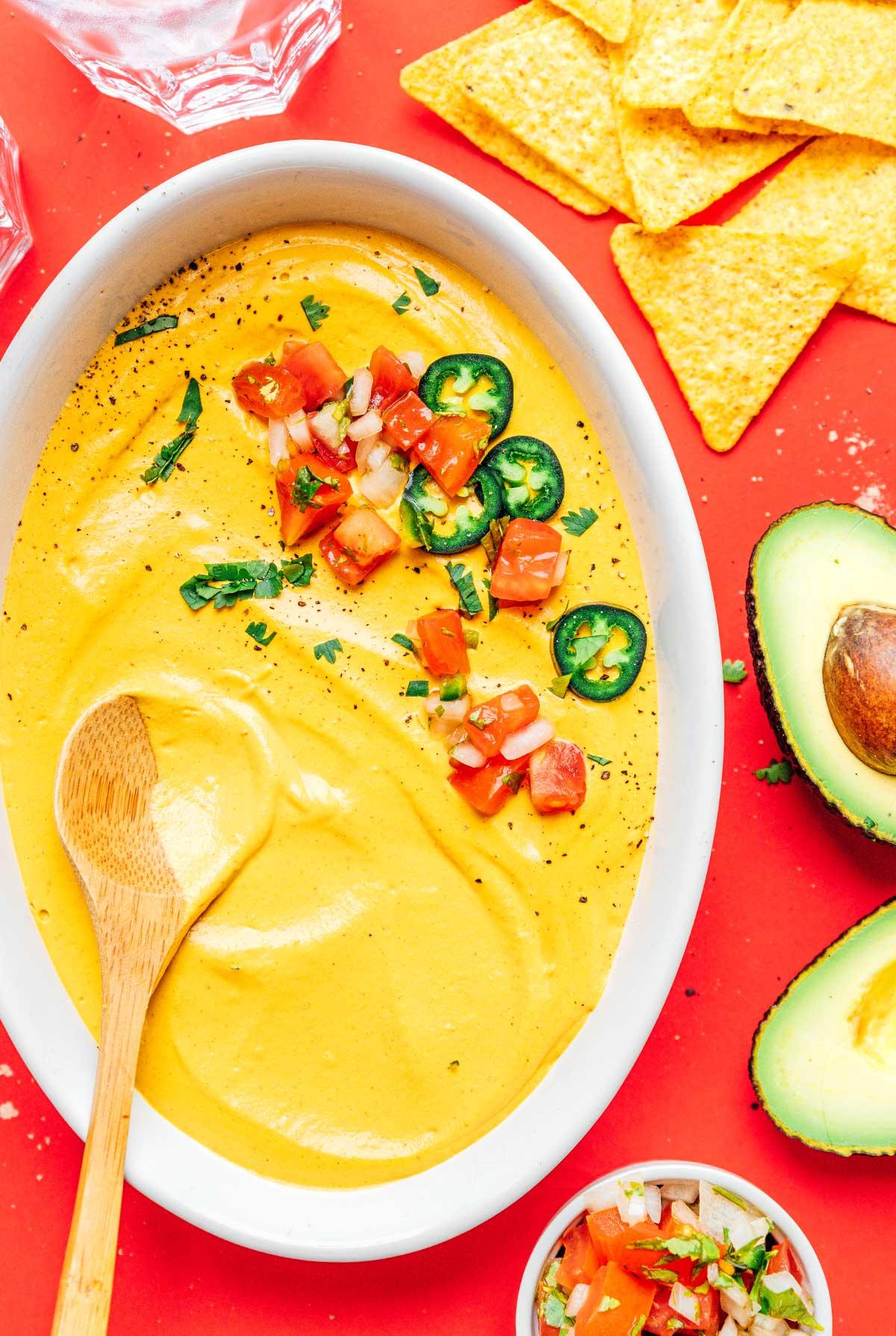 **10-Minuten-Rezept für veganen Queso** 2 Eine weiße Schüssel gefüllt mit veganem Queso, garniert mit Jalapeños, Tomaten und frischem Koriander, umgeben von köstlichen Taco-Zutaten.