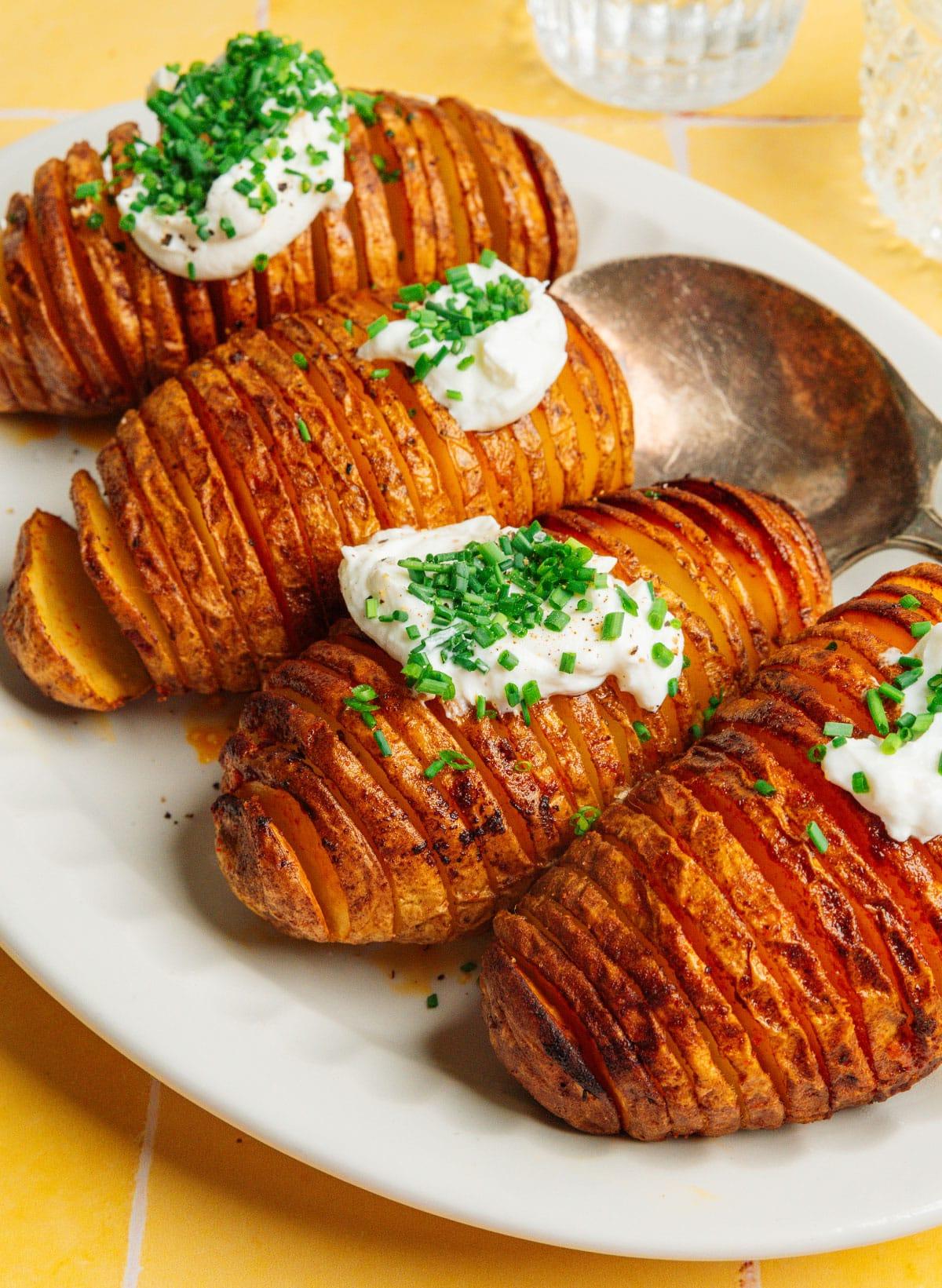 Heißluftfritteusen-Hasselback-Kartoffeln 2 Hasselback-Kartoffeln mit Sauerrahm und Schnittlauch auf einer Platte.