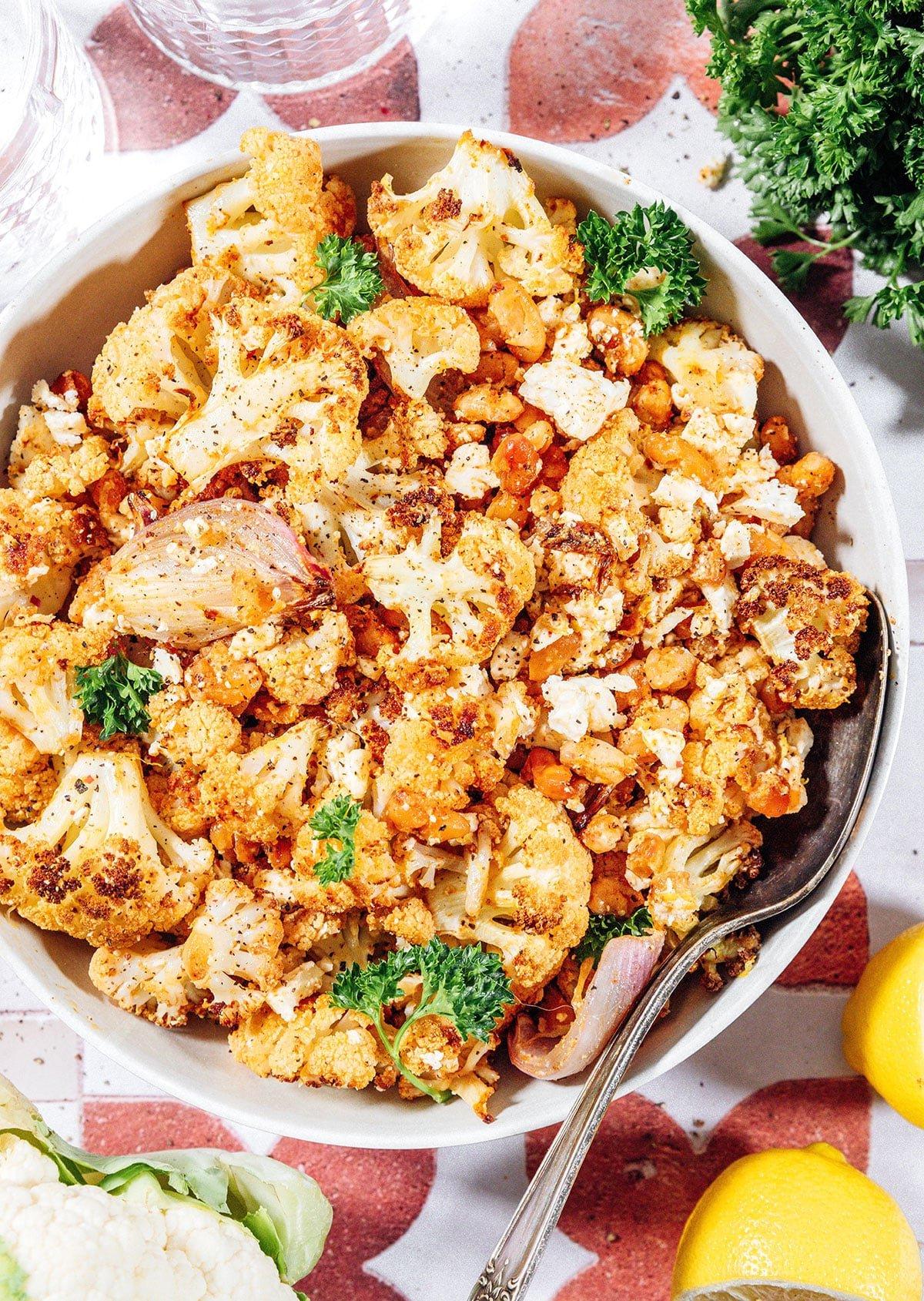 Gerösteter Blumenkohlsalat mit knusprigen Bohnen 2 Ein Teller mit geröstetem Blumenkohlsalat, garniert mit frischen Kräutern und Feta.