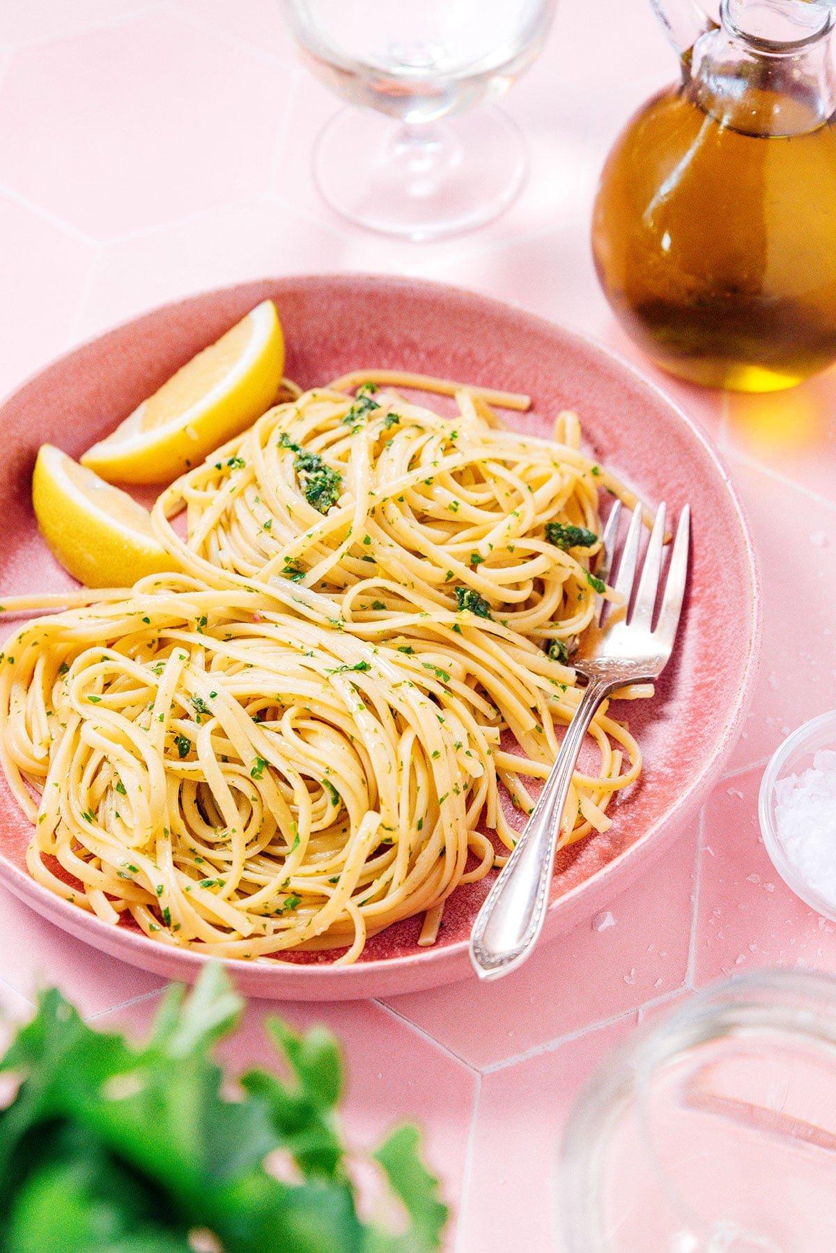 Zitronige Gremolata Pasta (Fertig in 15 Minuten) 2 Eine flache rosa Schüssel gefüllt mit mediterraner Pasta und zwei Zitronenspalten