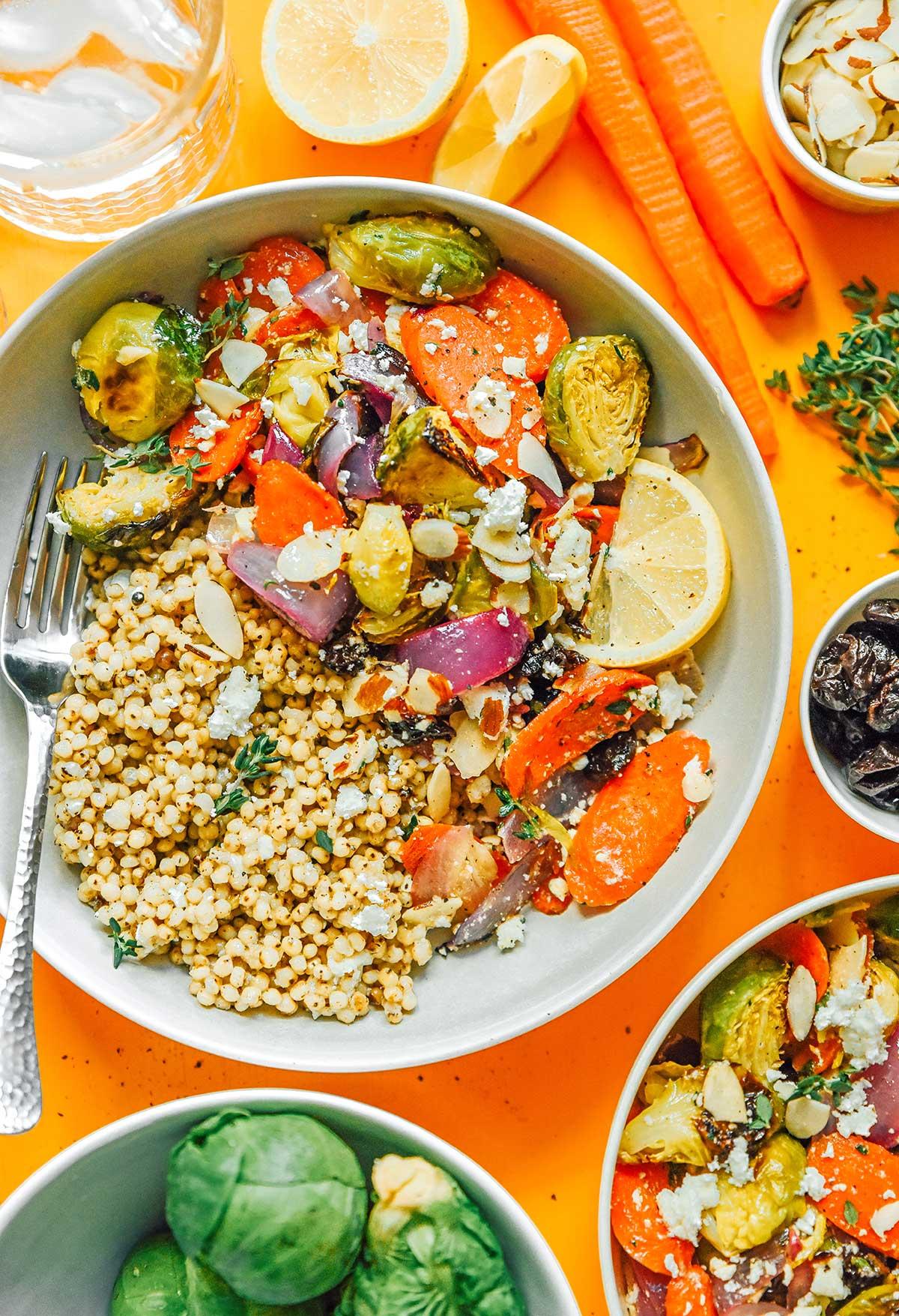 Geröstete Gemüse-Getreide-Bowls 2 Eine Getreide-Bowl mit geröstetem Gemüse, gefüllt mit Seitan, roter Zwiebel, Rosenkohl, Karotten, Zitronenscheiben, Feta-Käse und mehr.