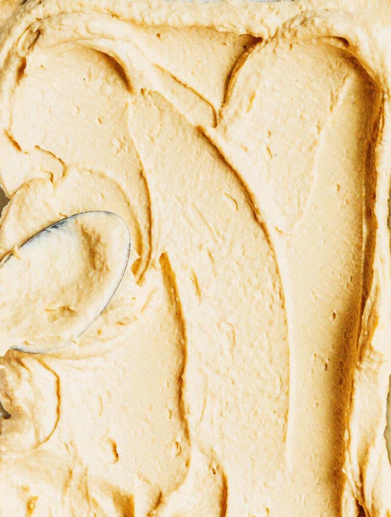 **10 Arten, Hummus zu essen (+ Rezepte!)** 2 Ein Löffel verteilt Hummus auf einer Oberfläche – Nahaufnahme.