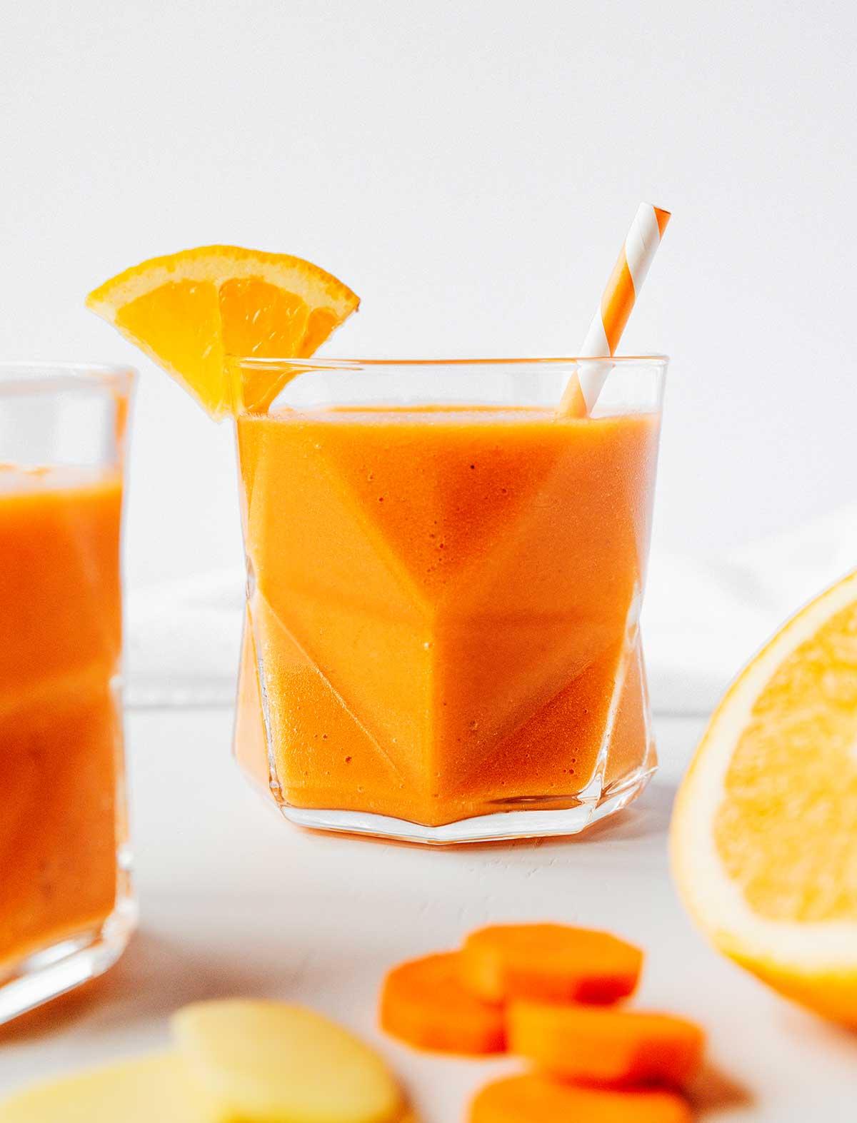 Ein Glas gefüllt mit frisch gemischtem Karotten-Smoothie mit Zitrusfrüchten und Ingwer, garniert mit einer Orangenscheibe