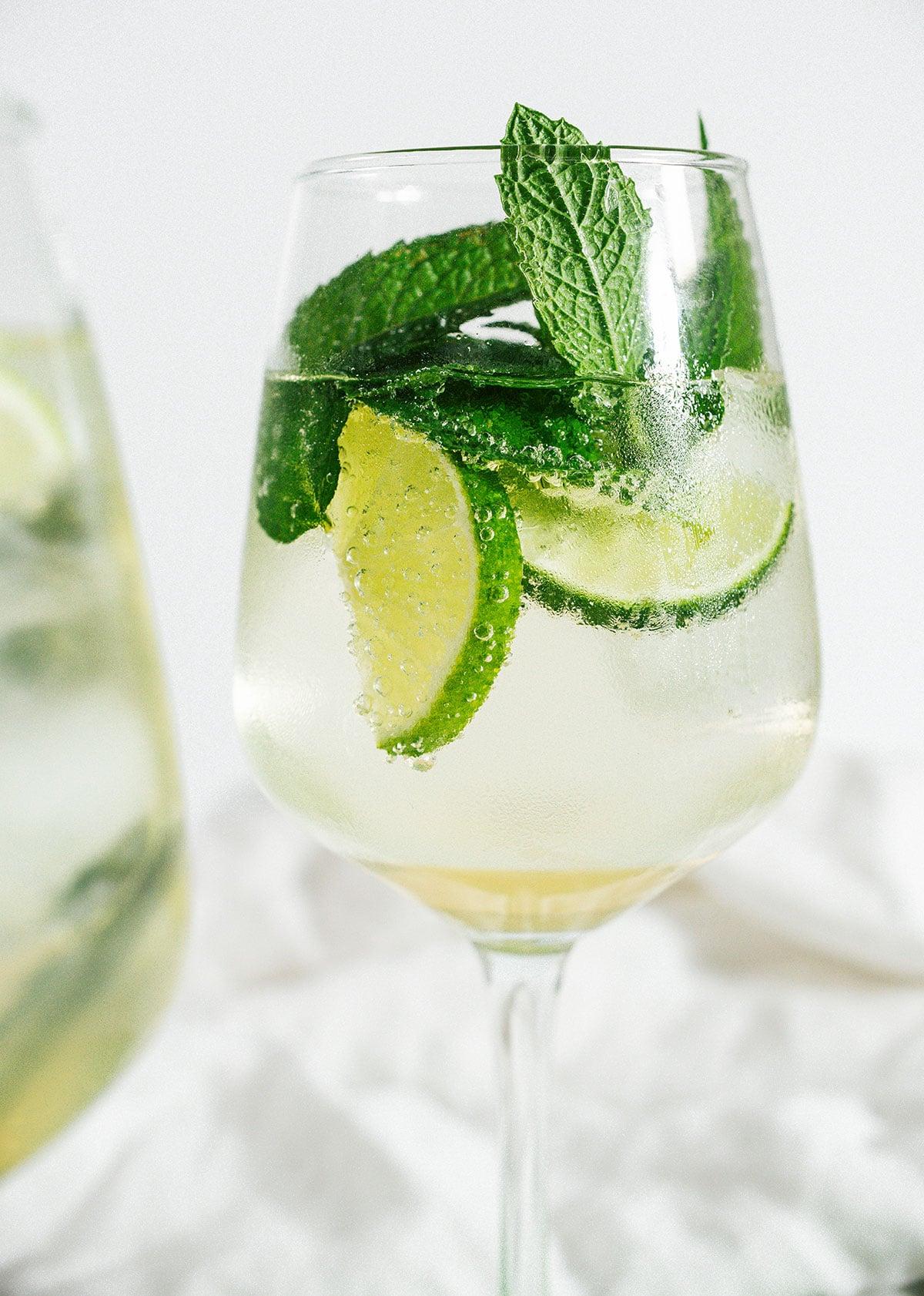 Vegetarische 31-Tage-Herausforderung 11 Hugo Spritz Cocktail in einem Glas mit Limettenscheiben und frischer Minze.