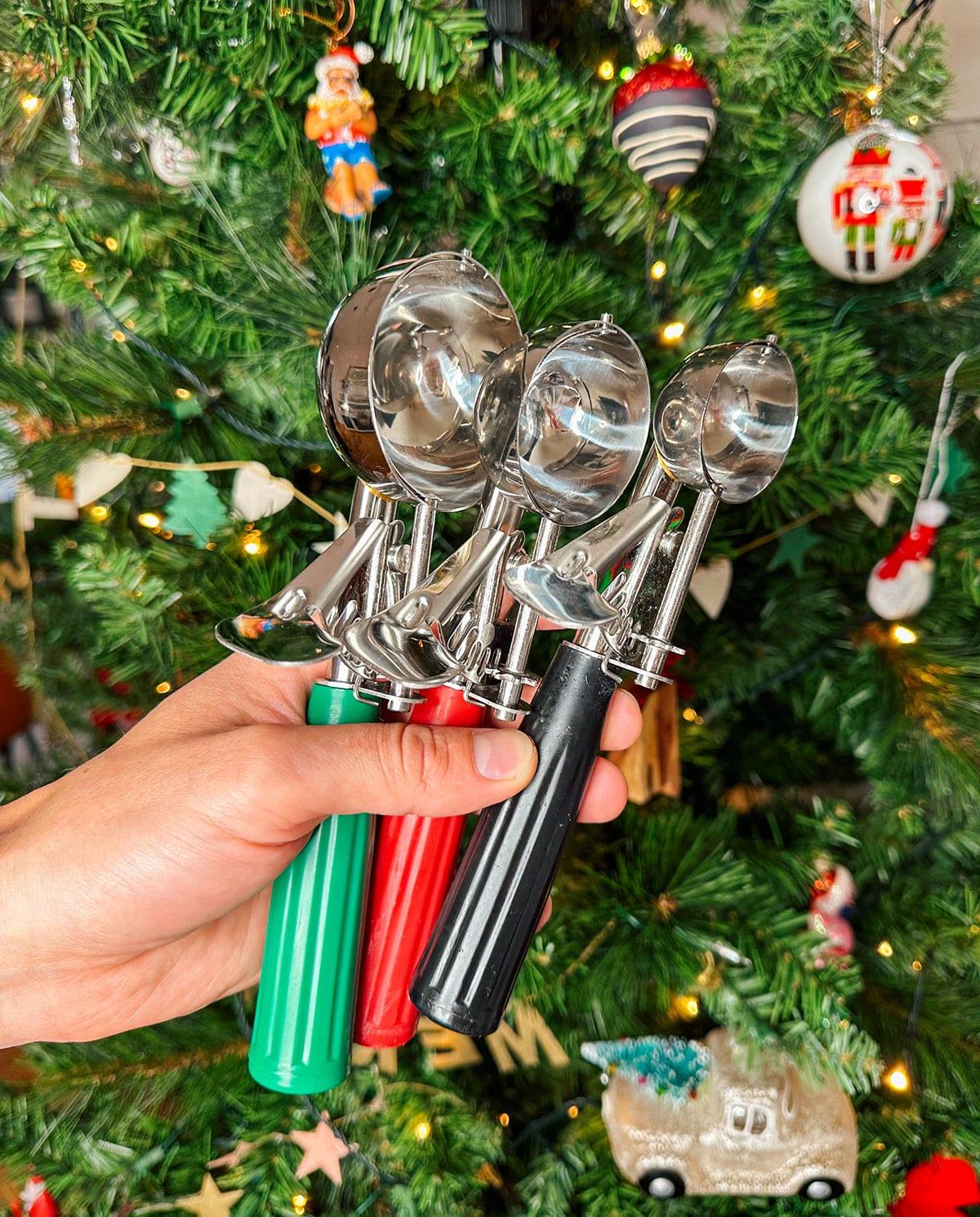Verschiedene Portionierlöffel als Geschenk vor einem Weihnachtsbaum.