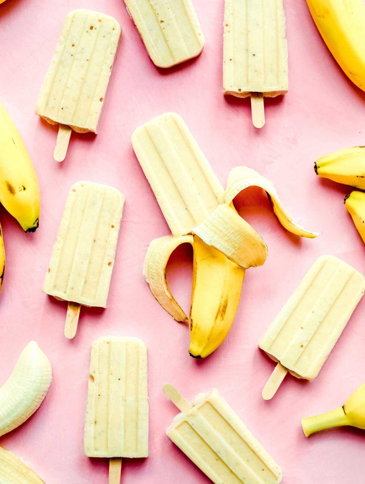 Bananen-Popsicles und ganze Bananen bilden ein spielerisches Muster auf einem leuchtend pinken Hintergrund.