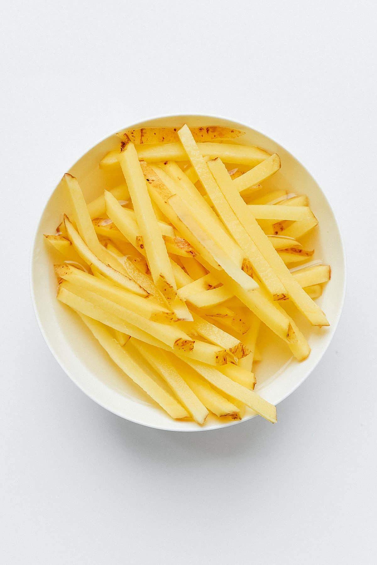 Heißluftfritteusen-Kartoffeln: Der ultimative Leitfaden 11 Pommes Frites weichen in einer Schüssel Wasser ein.