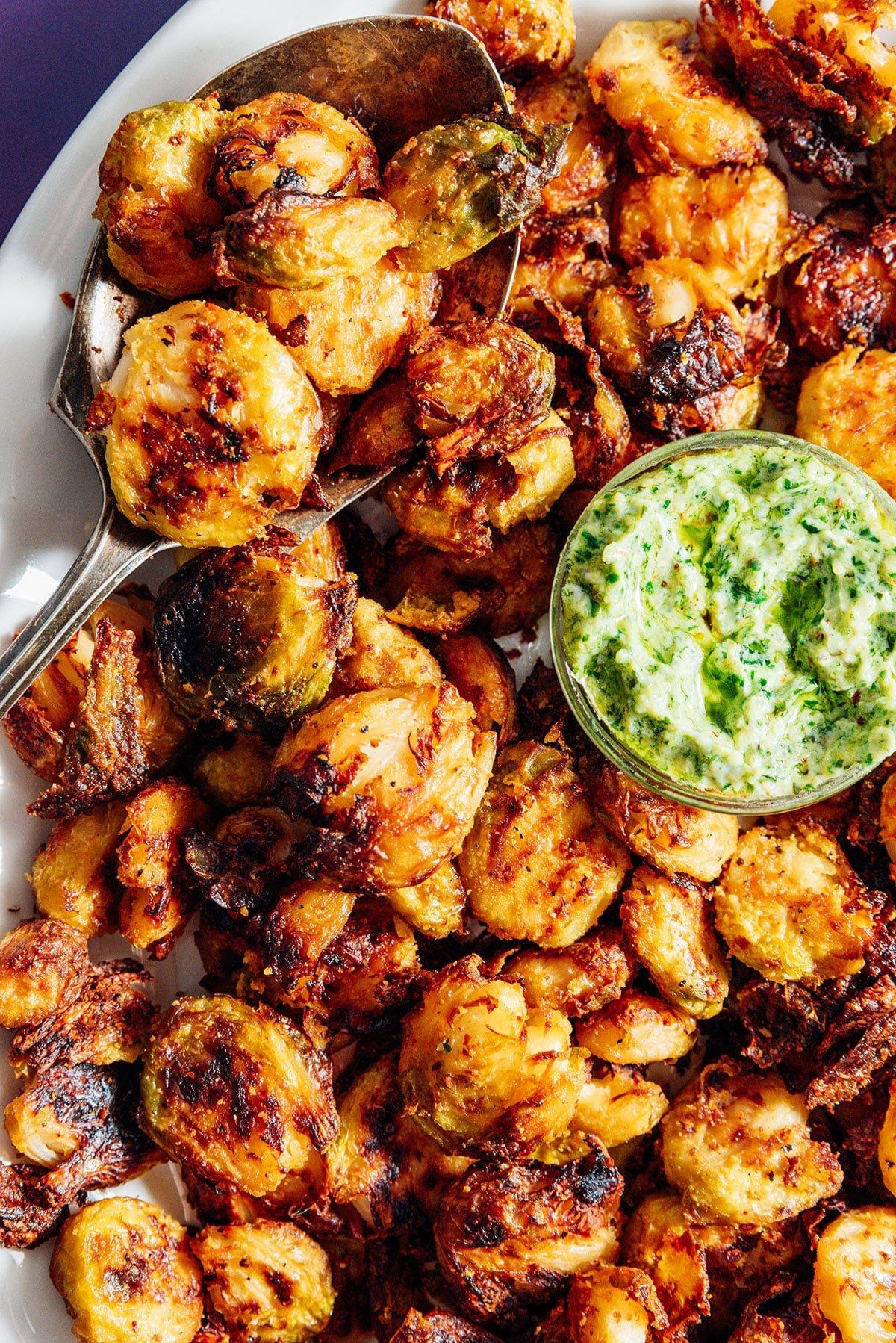 TikTok-viraler knuspriger zerdrückter Rosenkohl 11 Knuspriger zerdrückter Rosenkohl auf einer Platte mit grüner Pesto-Mayo-Sauce, Nahaufnahme.
