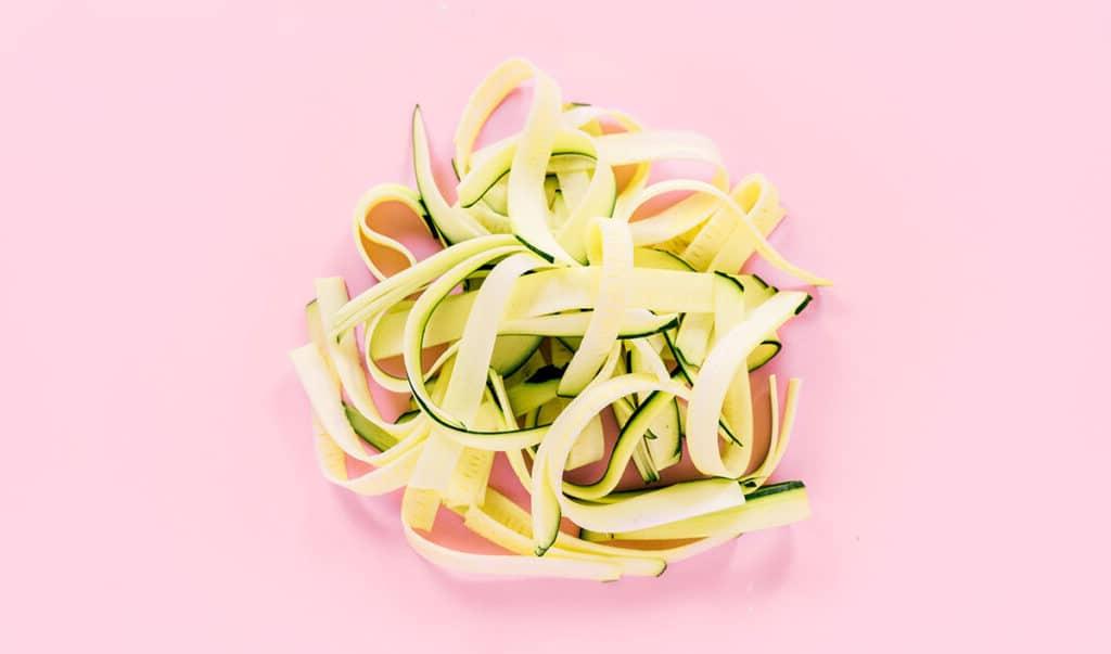 Zucchininudeln zubereiten 12 Ein Stapel Fettuccine-Zucchini-Nudeln auf rosafarbenem Hintergrund.