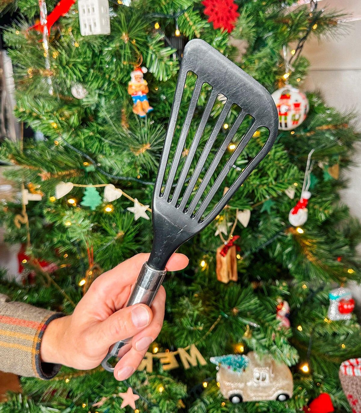 Ein flexibler Fischpfannenwender als Geschenk vor einem Weihnachtsbaum.