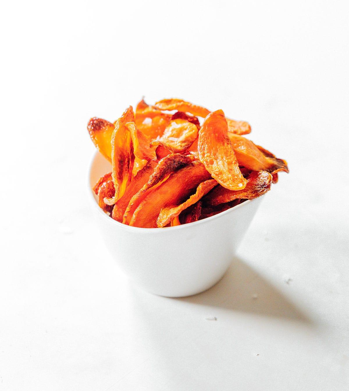 Ofengebackene Karotten-Chips 12 Karottenchips mit grobem Meersalz in einer weißen Tasse.