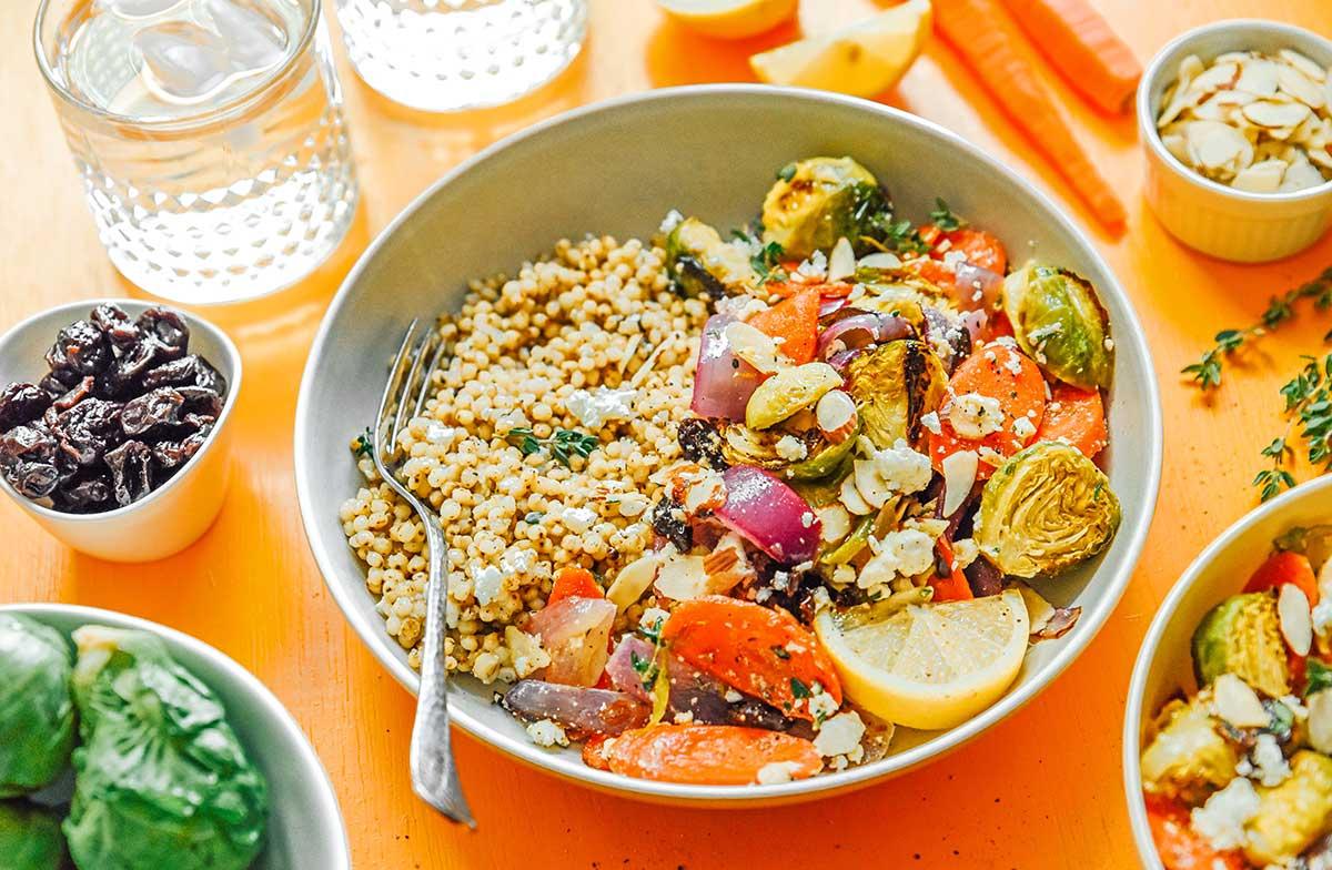 Geröstete Gemüse-Getreide-Bowls 12 Eine geröstete Gemüse-Getreide-Bowl gefüllt mit Seitan, roter Zwiebel, Rosenkohl, Karotten, Zitronenscheiben, Feta-Käse und mehr.