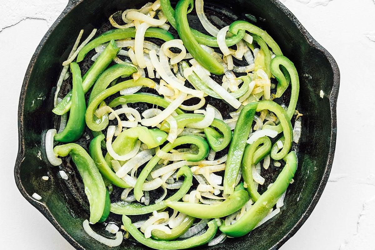 Grüne Paprika und Zwiebeln in einer gusseisernen Pfanne.