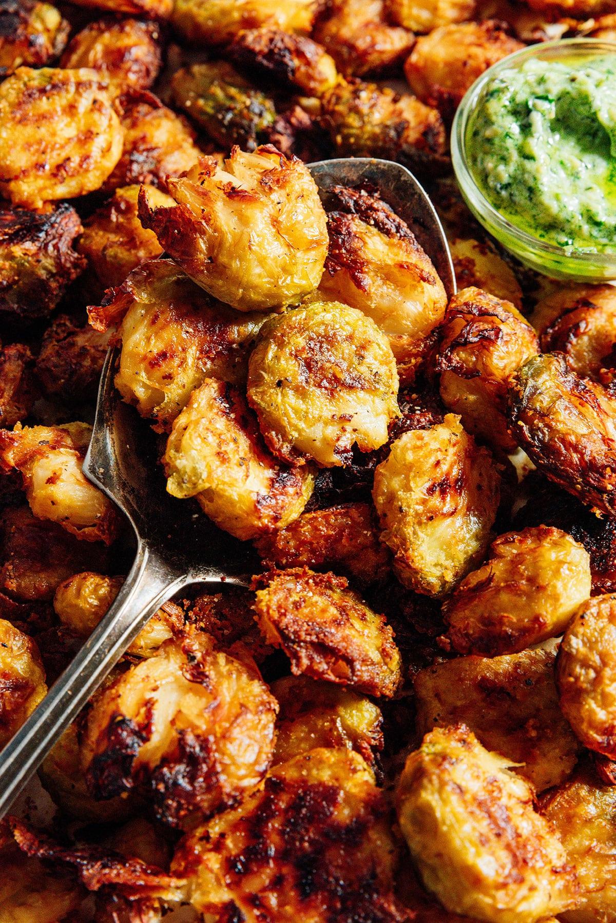 TikTok-viraler knuspriger zerdrückter Rosenkohl 12 Knuspriger zerdrückter Rosenkohl auf einer Platte mit grüner Pesto-Mayo-Sauce, servierfertig.