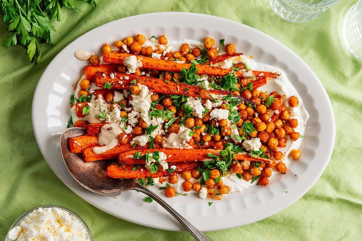 Der fertige Teller mit gerösteten Karotten, knusprigen Kichererbsen und Tahini-Sauce, garniert und servierfertig.