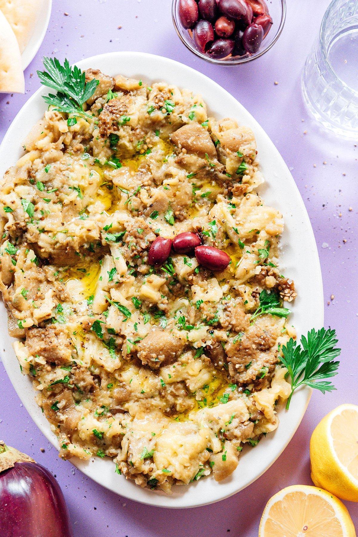 Griechischer Auberginen-Dip (Melitzanosalata) 13 Nahaufnahme eines texturierten griechischen Auberginen-Dips auf einer weißen Servierplatte.