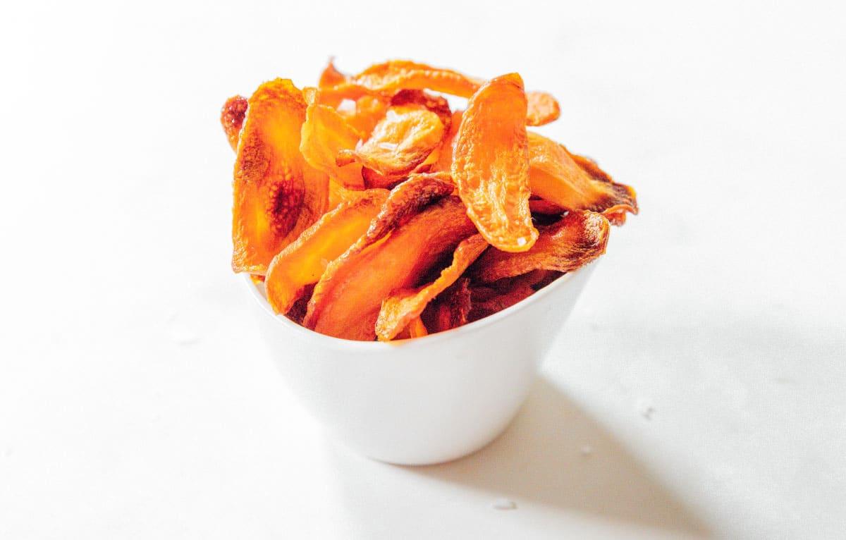 Ofengebackene Karotten-Chips 13 Karottenchips mit grobem Meersalz in einer weißen Tasse.