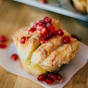 Orangen-Granatapfel Zupfbrot (2 Arten) 14 Ein Gebäck, gekrönt mit leuchtend roten Granatapfelkernen, liegt elegant auf einem kleinen Papierquadrat, die rustikale Holzoberfläche ist ebenfalls mit weiteren Kernen übersät. Dieses verlockende Zupfbrot ist sowohl ein Fest für die Augen als auch ein unwiderstehlicher Genuss für Ihre Geschmacksnerven.