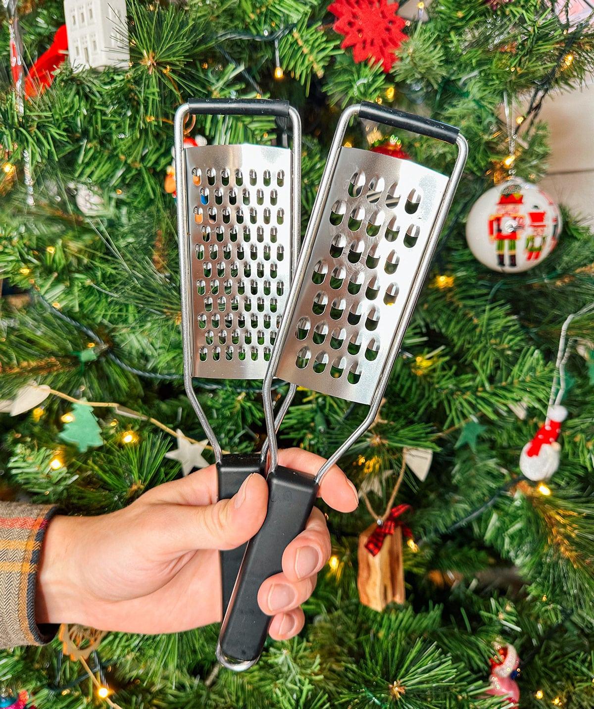 Verschiedene Käsereiben als Geschenk vor einem Weihnachtsbaum.