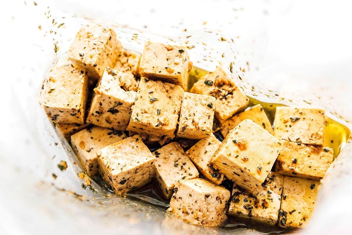 Wie man Tofu mariniert (8 Geschmacksrichtungen!) 17 Tofu-Würfel und Balsamico-Kräuter-Marinade in einem wiederverschließbaren Beutel.