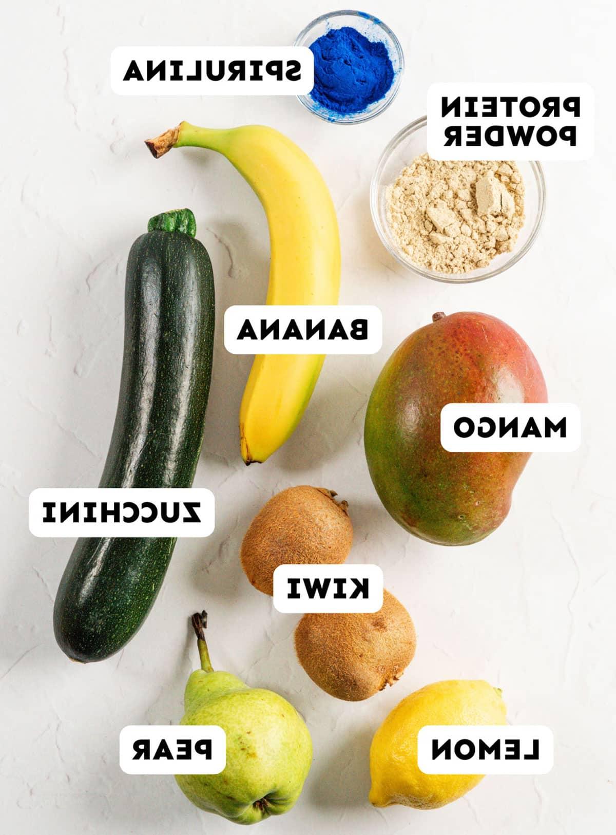 Smoothie-Würfel (Evive-Kopie) 18 Sortierte frische Früchte und Gemüse, Proteinpulver, Spirulina-Pulver und Smoothie-Würfel sind auf einer weißen Oberfläche angeordnet, jeweils beschriftet: Mango, Kiwi, Zitrone, Birne, Banane, Zucchini, Proteinpulver, Spirulina.