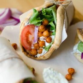 A chickpea gyros pita wrap brimming with roasted chickpeas, crisp lettuce, juicy tomato, and tangy red onion, all elegantly tied with twine on a parchment sheet.