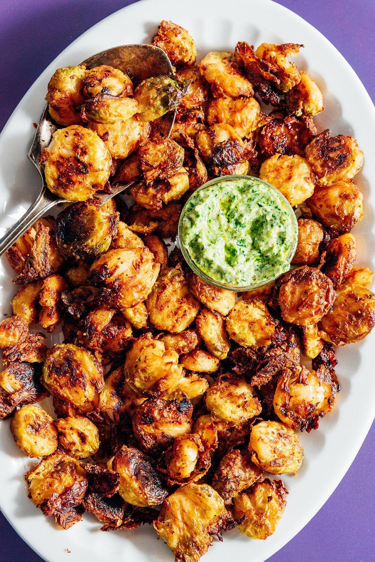 TikTok-viraler knuspriger zerdrückter Rosenkohl 3 Knuspriger zerdrückter Rosenkohl auf einer Platte mit grüner Pesto-Mayo-Sauce, Nahaufnahme.