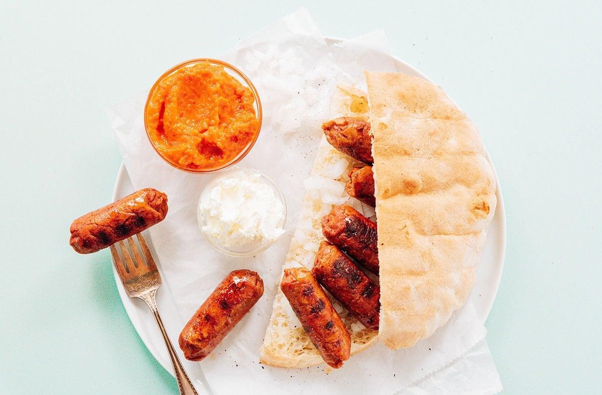 Vegetarische Cevapcici (Kroatisches Cevapi-Sandwich-Rezept) 3 Vegetarische Cevapi auf einem Teller mit Ajvar und Kajmak.