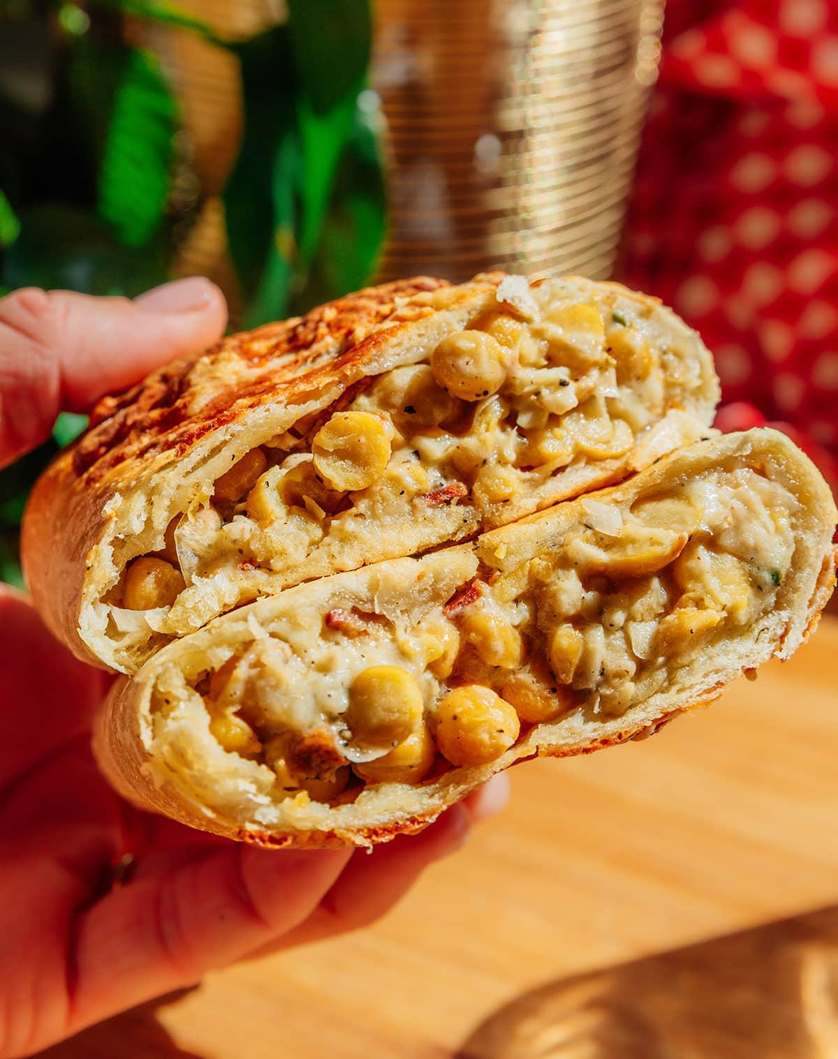Vegetarischer Costco „Hähnchen“-Auflauf (Mit Kichererbsen!) 3 Nahaufnahme einer Hand, die eine halbierte Rolle hält, gefüllt mit Kichererbsen und cremiger Sauce. Die Füllung ist reichhaltig und gut sichtbar, was die appetitliche Textur des Gerichts hervorhebt.