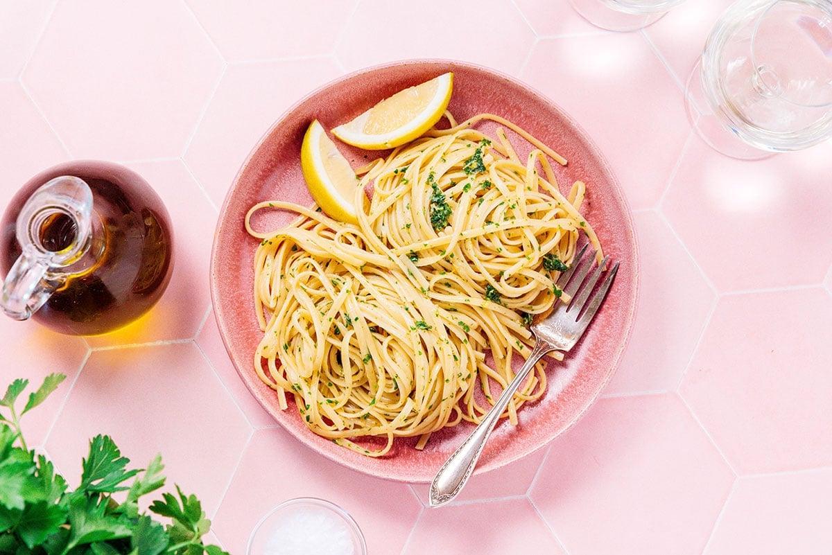 Zitronige Gremolata Pasta (Fertig in 15 Minuten) 3 Eine rosa Schüssel gefüllt mit Zitronen-Knoblauch-Pasta und zwei Zitronenspalten
