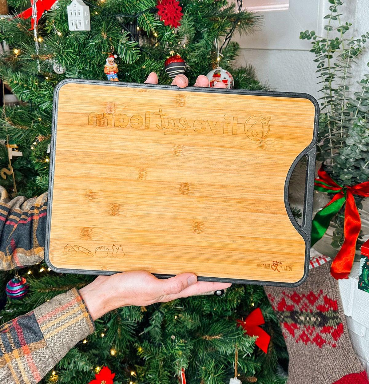 Ein persönlich graviertes Schneidebrett als Geschenk vor einem Weihnachtsbaum.