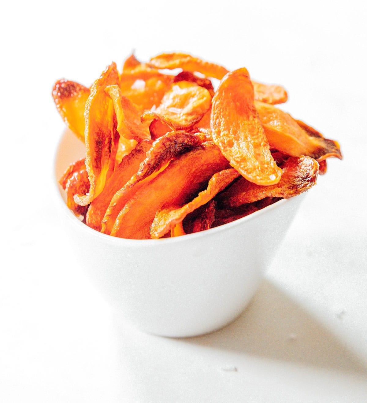Ofengebackene Karotten-Chips 3 Karottenchips mit grobem Meersalz in einer weißen Tasse.