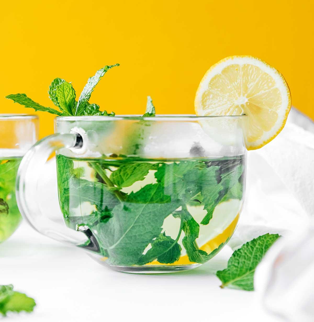 Frischer Minztee in einem klaren Glas, garniert mit Zitrone und Minze