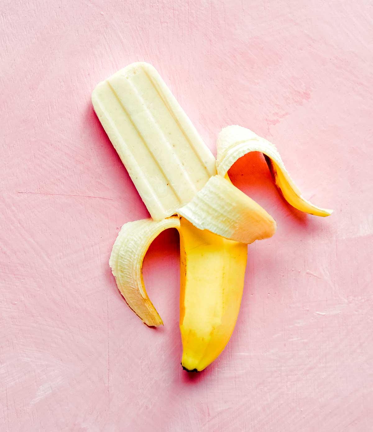 Bananen-Eis am Stiel aus 3 Zutaten 3 Ein Bananen-Popsicle kommt auf einer Bananenschale auf einem pinkfarbenen Hintergrund hervor.
