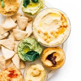 **10 Arten, Hummus zu essen (+ Rezepte!)** 3 Schüssel mit Regenbogen-Hummus-Sorten auf weißem Hintergrund.