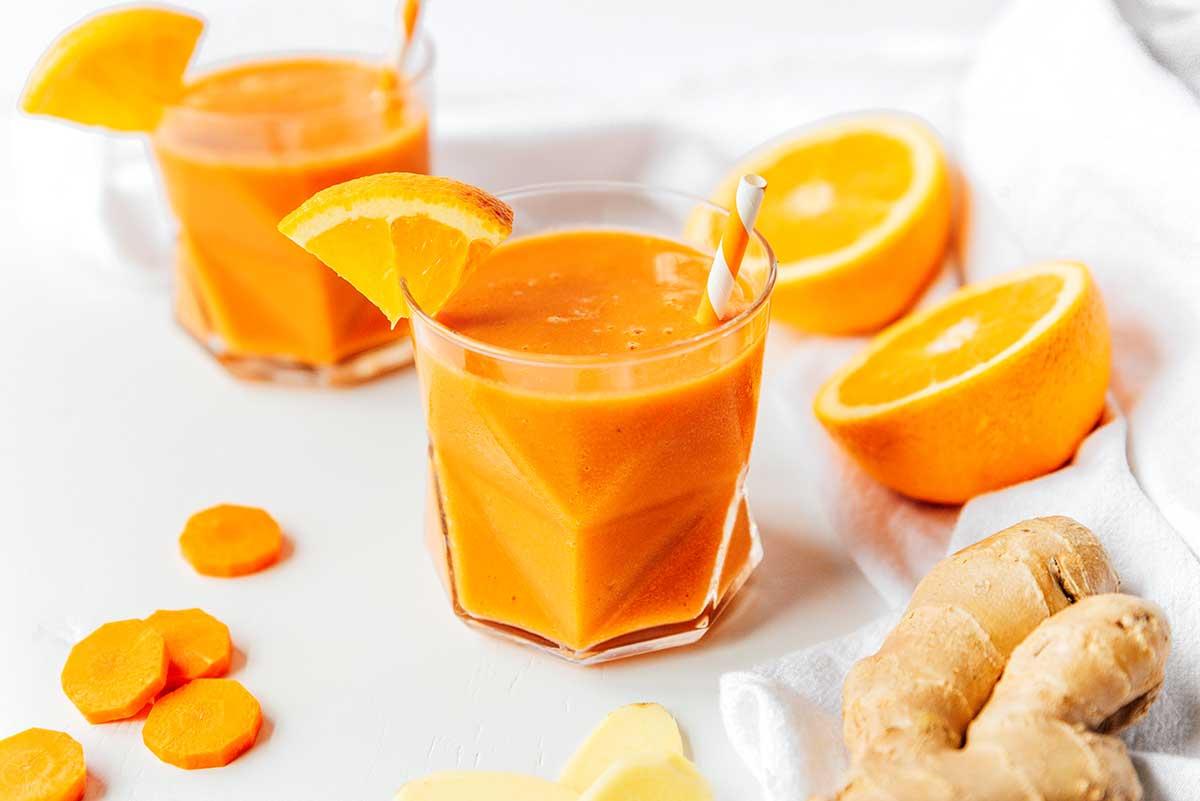 Ein Glas gefüllt mit frisch gemischtem Karotten-Smoothie mit Zitrusfrüchten und Ingwer, garniert mit einer Orangenscheibe
