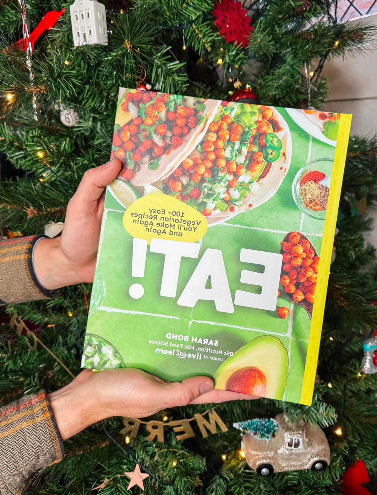 Mein vegetarisches Kochbuch 'Eat!' als Geschenk vor einem Weihnachtsbaum.