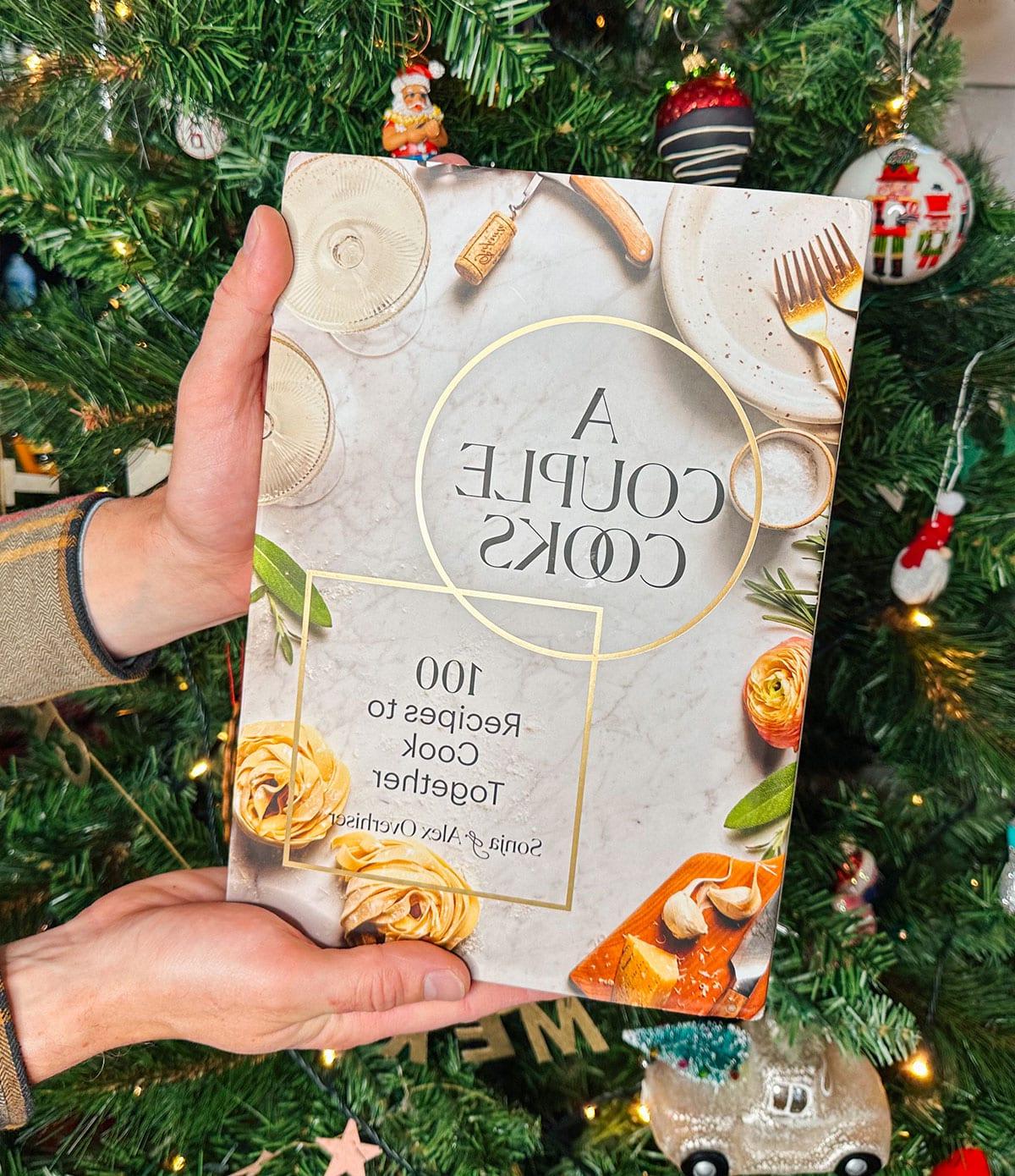 Das Kochbuch 'A Couple Cooks' als Geschenk vor einem Weihnachtsbaum.