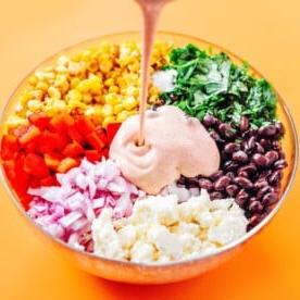 Pouring sauce into a bowl of elote salad
