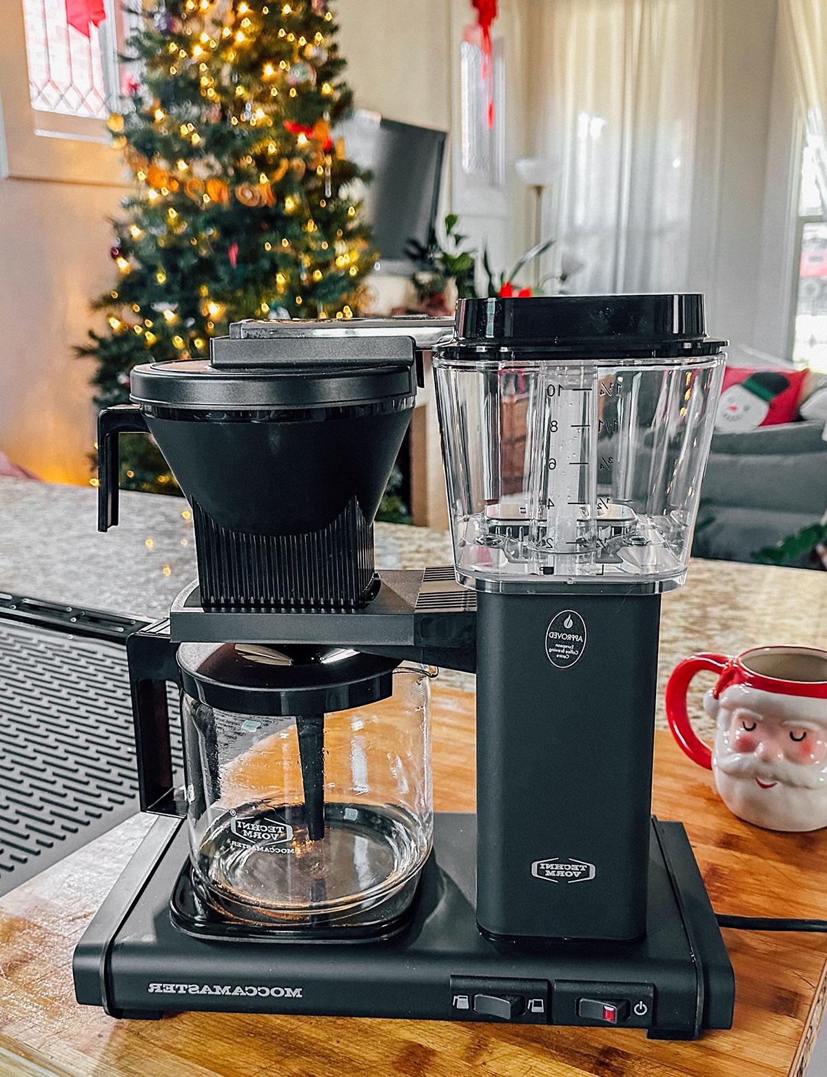 Eine Moccamaster Kaffeemaschine als Geschenk vor einem Weihnachtsbaum.