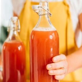 Girl in yellow overalls holding bottle of kombucha.