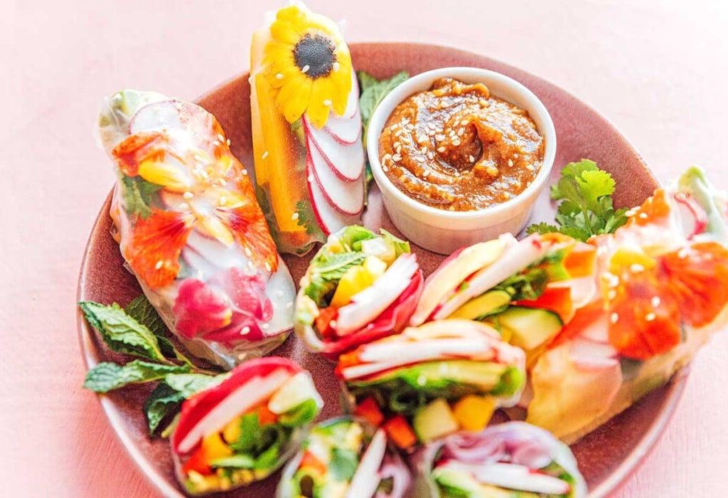 Essblumen-Frühlingsrollen 4 Eine rosa Schale gefüllt mit neun essbaren Blüten-Sommerrollen und einer kleineren Schale mit Mandelbutter-Dip-Sauce