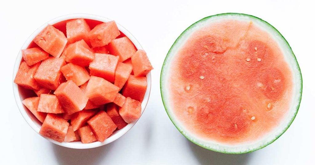 Einfache Wassermelonen-Granita 4 Halbe Wassermelone mit gewürfelten Wassermelonenstücken auf einem weißen Hintergrund