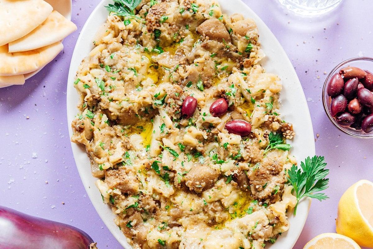 Griechischer Auberginen-Dip (Melitzanosalata) 4 Weiße Platte mit griechischem Auberginen-Dip, garniert mit Oliven, Öl und Kräutern.