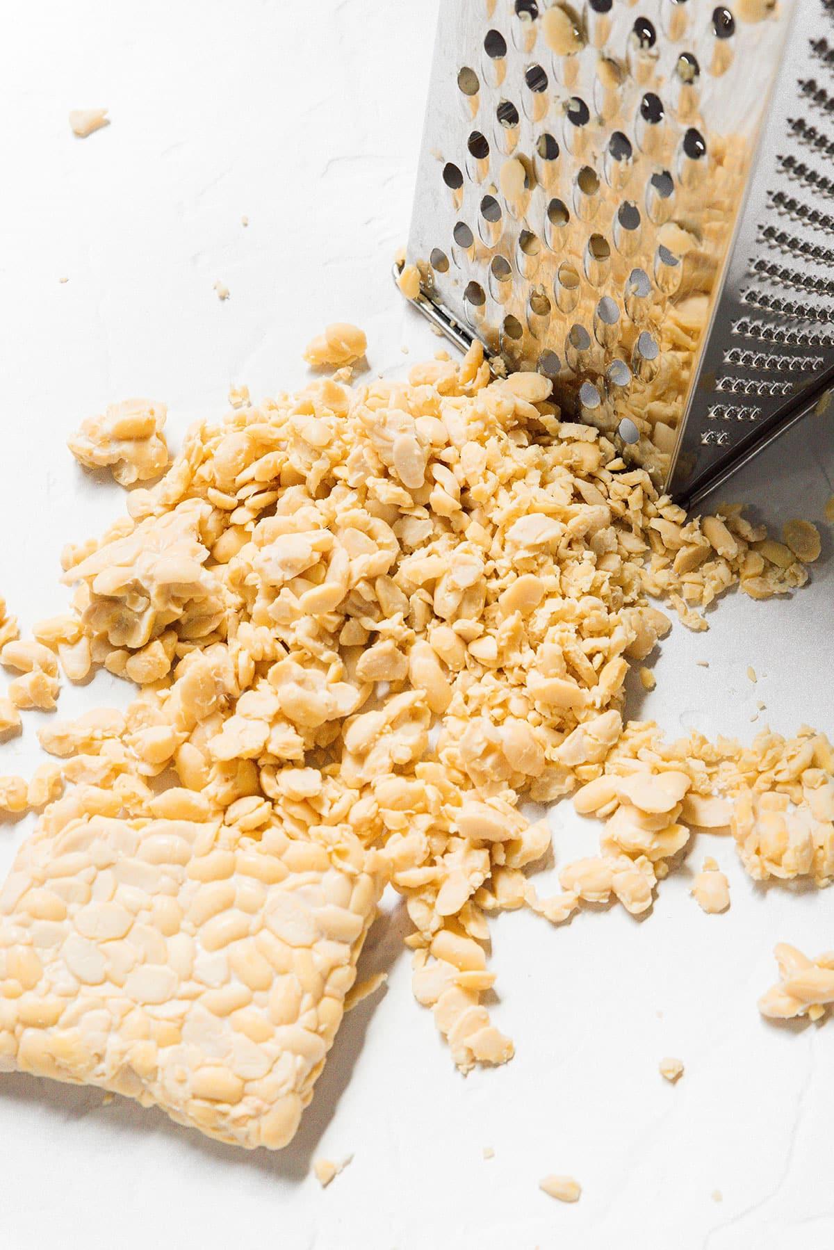 Tempeh Taco Fleisch 4 Ein Detailbild von Tempeh, das mit einer Kastenreibe geraspelt wird, um die Textur von Hackfleisch zu imitieren.