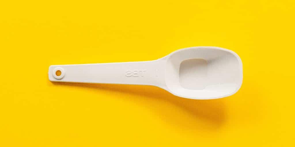 Wie viele Esslöffel sind in einer Tasse? (+ Umrechnungshilfe!) 4 Ein leerer weißer Plastik-Esslöffel auf einer gelben Oberfläche.