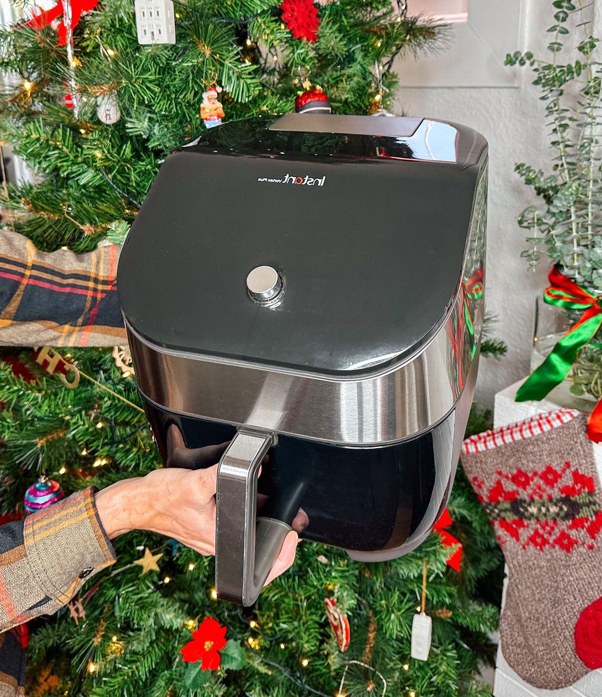 Eine Instant Vortex Heißluftfritteuse als Geschenk vor einem Weihnachtsbaum.